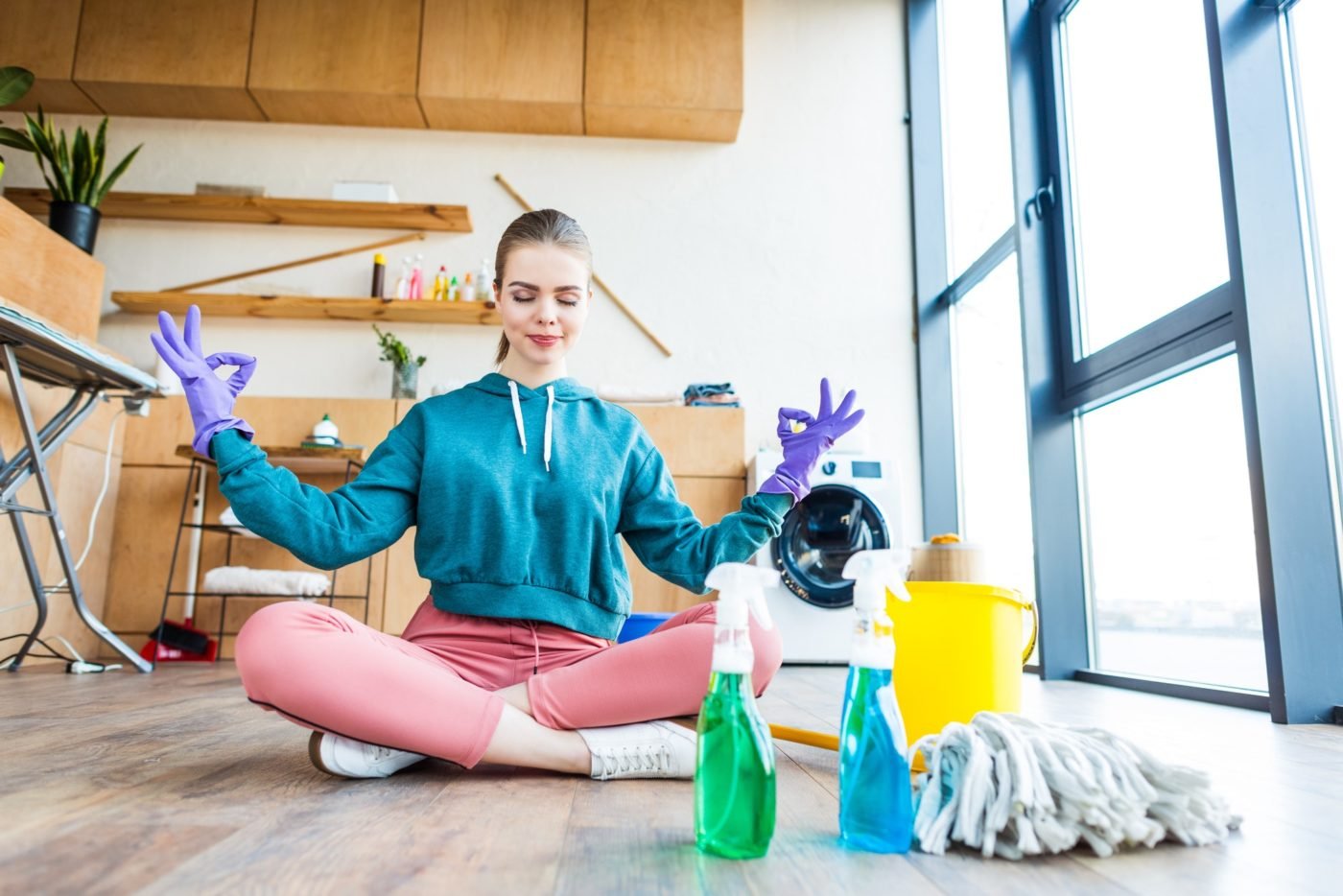 smiling-young-woman-sitting-on-floor-and-meditating-while-cleaning-house-e1669624929148
